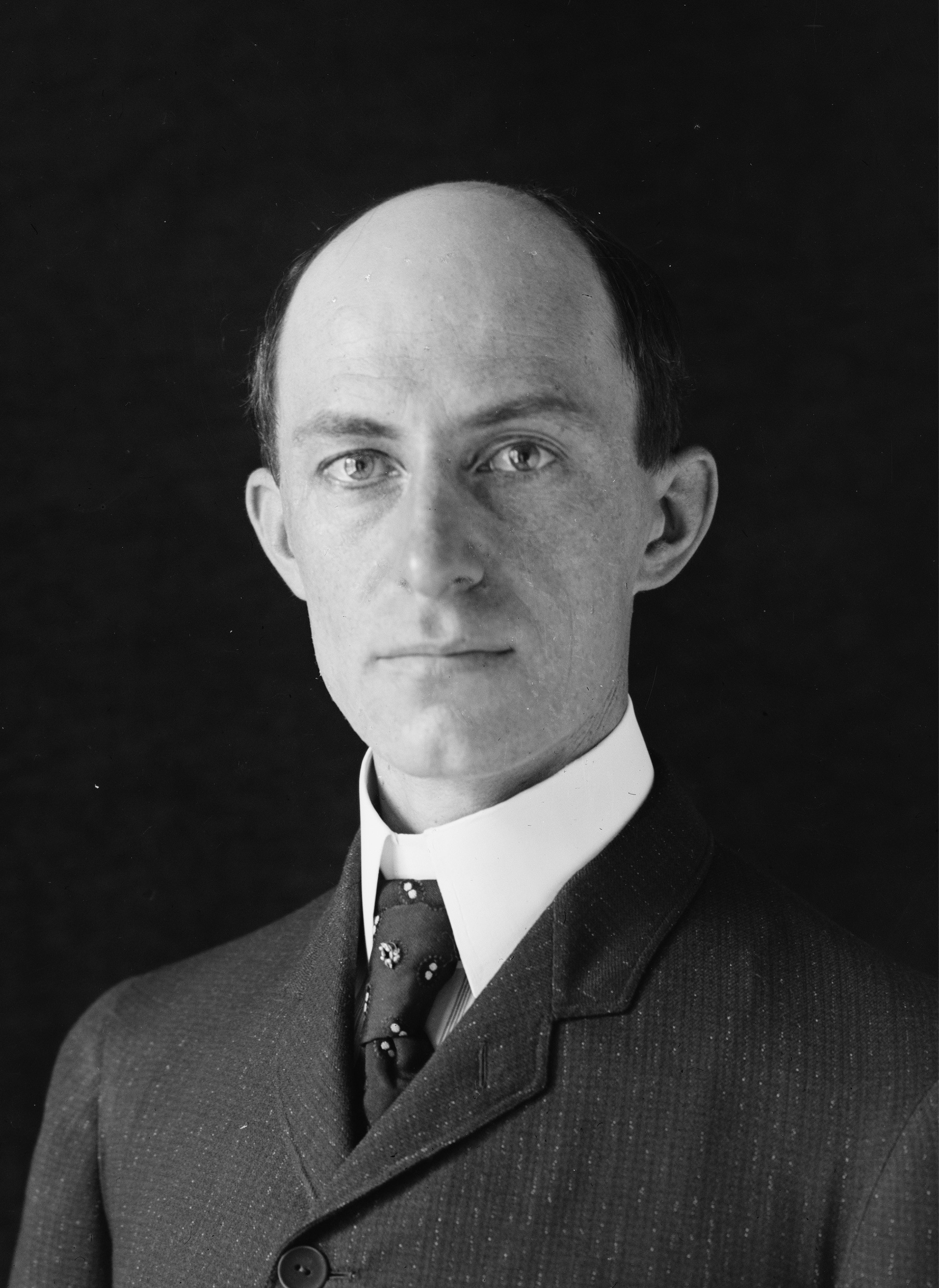 This is a photographic portrait of Wilbur Wright, the elder of the two famed Wright brothers. He is clean shaven, balding, and wears a suit and tie.